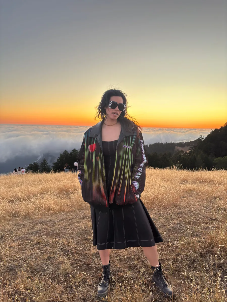 Someone wearing the Made You Look lenticular jacket on a golden hillside at sunset, fog rolling below.